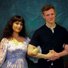 two people standing next to each other in front of a blue wall with green leaves