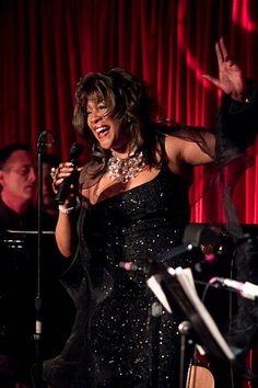 a woman in a black dress singing into a microphone