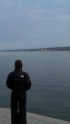 a woman standing on the edge of a pier looking out at the water