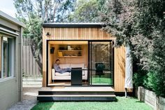 a man sitting in the back of a small house on top of some grass next to trees