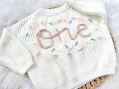 a white sweater with the word gone written in pink and blue sprinkles