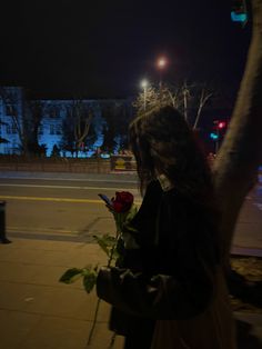 a woman standing on the sidewalk holding a rose