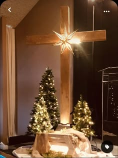 a wooden cross with christmas trees in front of it and lights on the ground next to it