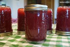 four jars filled with red liquid sitting on top of a green and white checkered table cloth