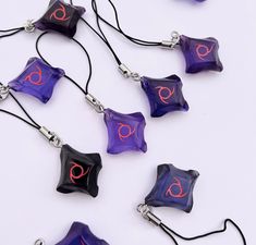 purple and black glass necklaces with pink letters on them, hanging from cords against a white background