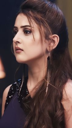 a woman with long brown hair wearing large hoop earrings and black dress looking off to the side