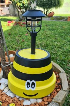 a yellow and black bee lamp sitting on top of a flower pot filled with rocks