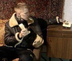 a person sitting on a couch with a phone in their hand and wearing a leather jacket