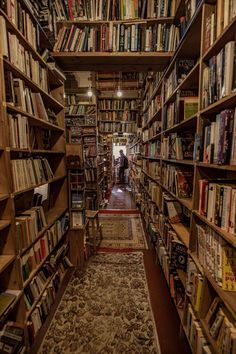 a narrow bookshelf filled with lots of books and people in the distance walking through it