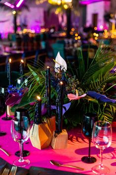 a table topped with lots of candles and vases filled with plants next to wine glasses