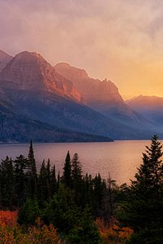 the sun is setting over a mountain lake with pine trees in front of it and mountains in the background