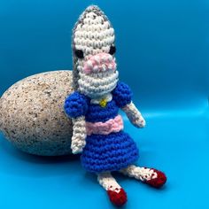 a crocheted stuffed animal sitting next to a rock on a blue tablecloth