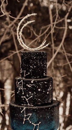 a three tiered black cake sitting on top of a table next to a tree