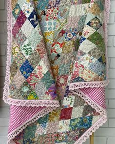 an old quilt hanging on a clothes rack in front of a white brick wall with pink trim