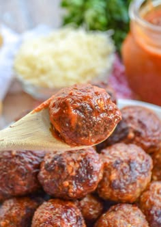 a wooden spoon full of meatballs with sauce on the side and breadcrumbs in the background