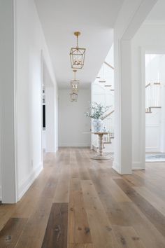 a white hallway with wood floors and chandelier hanging from the ceiling in front of it