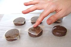 a hand reaching for chocolate covered doughnuts on wax paper with gold swirl designs