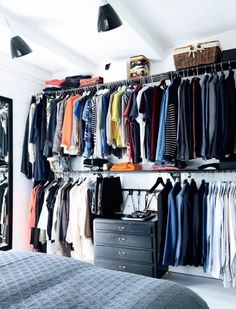 an organized closet with clothes hanging on the wall and drawers in front of it, next to a bed