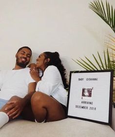 a man and woman laying on a bed next to a framed photo with the name of their baby