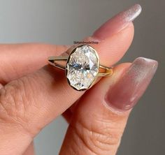 a woman's hand holding a ring with a large diamond in the middle of it