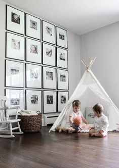 two young children playing in front of a teepee with pictures on the wall behind them