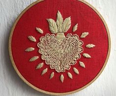 an embroidered heart on a red background with gold thread and leaves in the shape of a heart