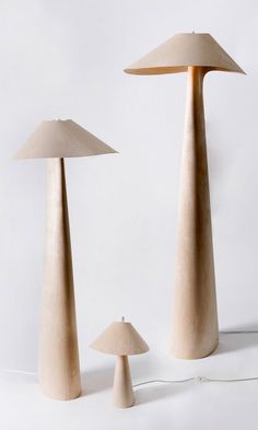 three tall wooden lamps sitting next to each other on a white surface with one lamp turned upside down