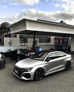 two silver cars parked in front of a building with a gas station on the other side