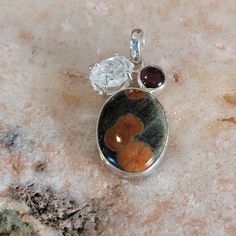 a silver pendant with an orange flower and two small stones on top of the necklace