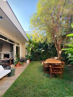 an outdoor patio with table and chairs next to a tree in the back yard, surrounded by greenery