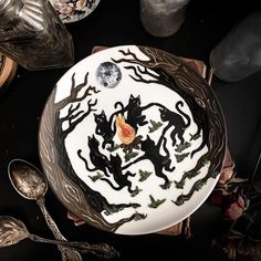 there is a cake decorated with cats and leaves on the plate next to spoons