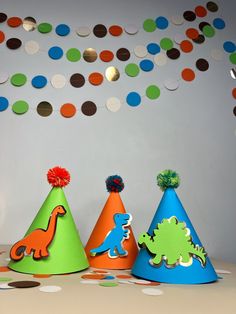 three party hats with dinosaurs on them and confetti hanging from the ceiling behind them