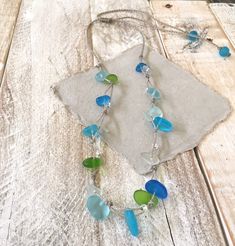 a necklace with blue and green glass beads on a white cloth covered piece of wood