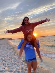 two girls standing on the beach with their arms out and one girl is holding her