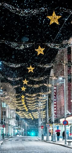 an empty city street is lit up with christmas lights and garlands on the buildings