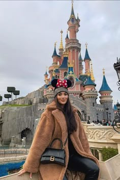 a woman is posing for a photo in front of the castle at disneyland world with minnie mouse ears on her head