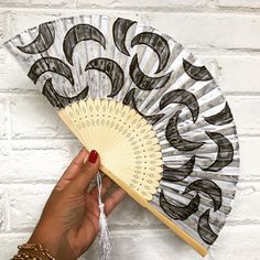 a hand holding a fan with black and white designs on it, against a brick wall