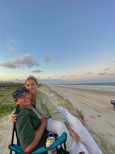 two people are sitting on a beach chair and posing for a photo with the ocean in the background