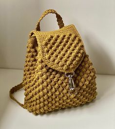 a crocheted yellow purse sitting on top of a white table next to a wall