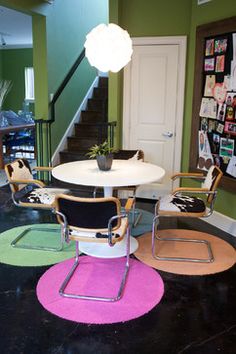 three chairs and a table in the middle of a room with green walls, carpeted floors and stairs