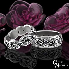 two wedding rings sitting next to each other on top of a black surface with pink flowers in the background