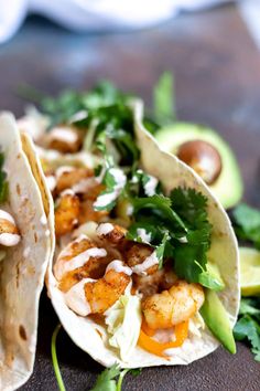 two tacos with shrimp, avocado and cilantro on them sitting on a table