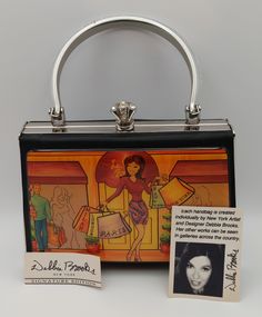 purse is a Debbie Brooks Signature Edition piece, created individually by the New York artist and designer. The front panel features a vibrant, stylized cityscape with figures engaged in shopping, highlighting a central figure holding bags labeled "PARIS." The background blends warm colors, giving a bustling city vibe. Debbie Brooks' works are showcased in galleries across the country, making this purse part of a limited-edition collection, which could be appealing to collectors and admirers of her art. Debbie Brooks' Signature Edition purses, like the one you have, were often released in the early 2000s. For example, some of her limited-edition pieces were created for events like the 2004 Tony Awards. Given the style and design, it's likely that your purse was made around that time period Artistic Rectangular Evening Bag, Bustling City, City Vibe, Vintage Purses, Tony Awards, Evening Clutch, Chic Boutique, Handbag Purse, New Yorker