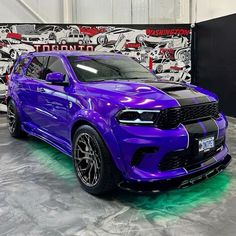 a purple car parked in front of a wall with graffiti on it's sides