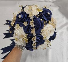 a bridal bouquet with blue, white and gold flowers is being held by someone's hand