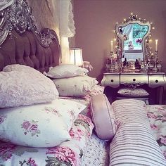 a bed covered in lots of pillows next to a table with a mirror on it