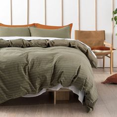 a bed with green and white comforters in a room next to a chair, potted plant