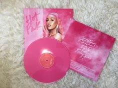 a pink vinyl record sitting on top of a white carpet next to an album cover