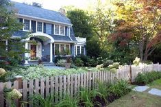 a house with a picket fence in front of it and lots of flowers around the yard