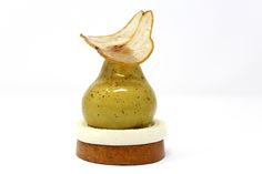 an apple slice is placed on top of a small green vase that sits on a white surface